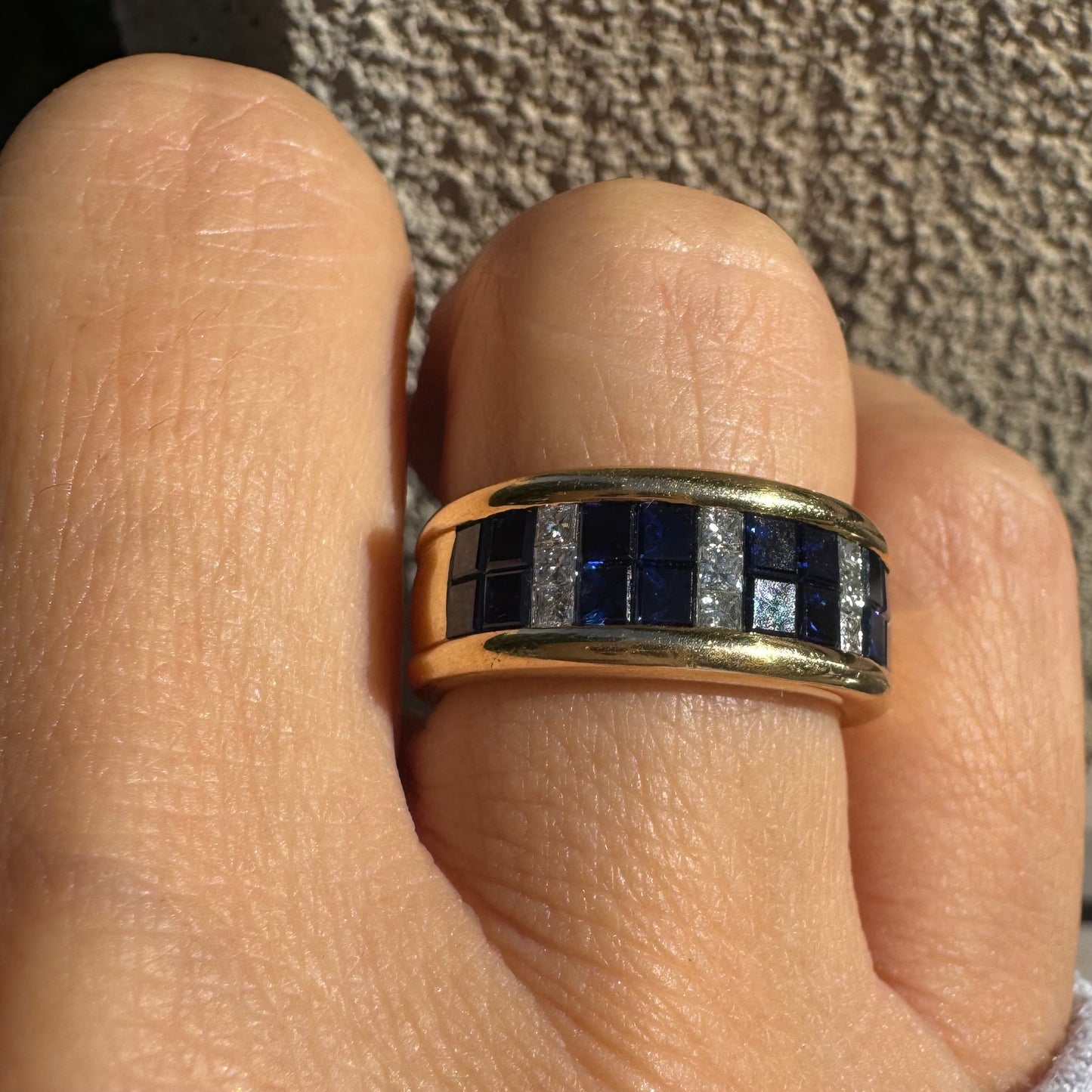 טבעת ה.שטרן זהב צהוב 18 קראט, בעיצוב רחב ומרשים. משובצת שורת אבני ספיר כחולות מרובעות בשילוב מחיצות של יהלומים לנגיעת ברק יוקרתי.