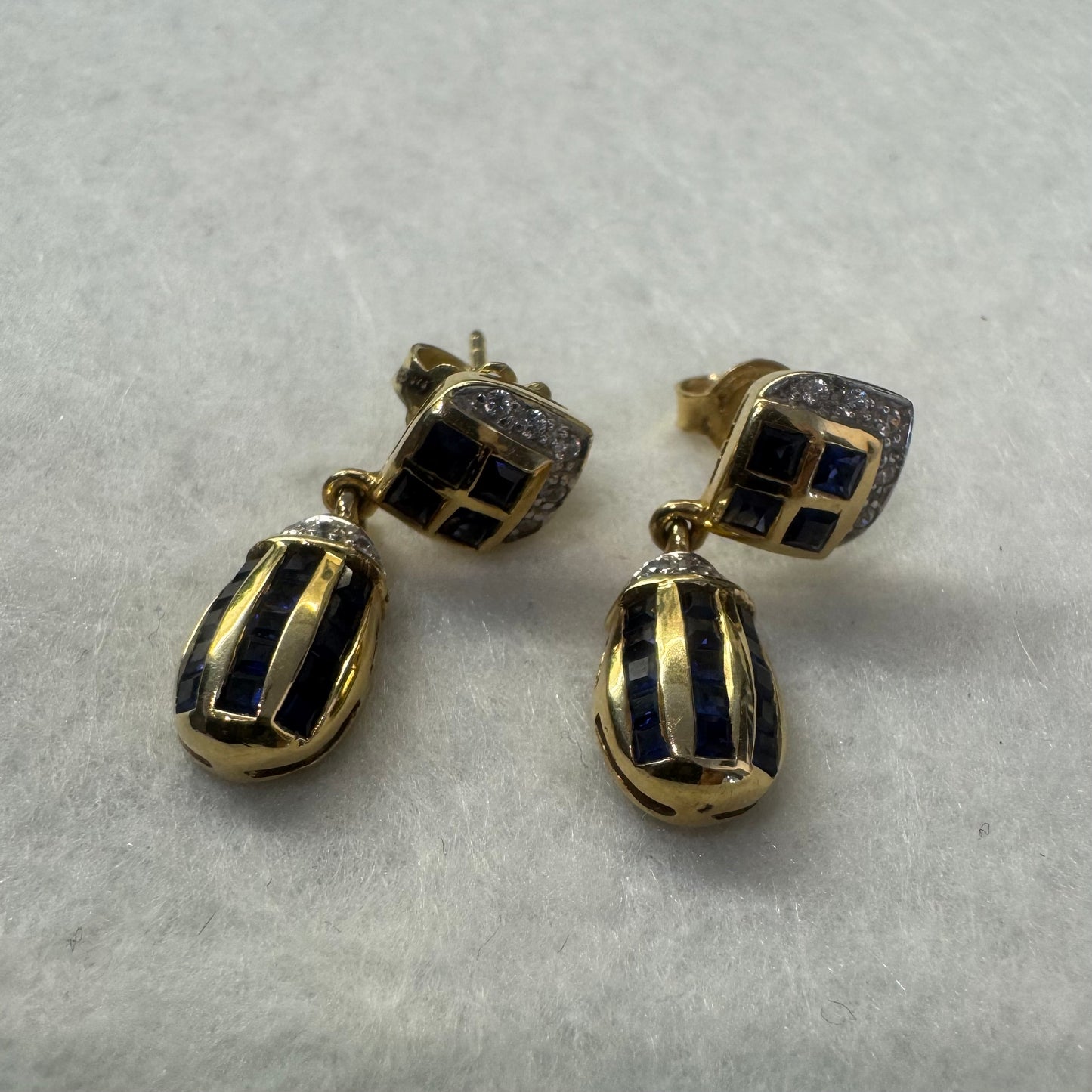 עגילי זהב צהוב 18 קראט תלויים, משובצים אבני ספיר כחולות בגוון כחול עמוק בעיצוב גיאומטרי, בשילוב יהלומים מנצנצים