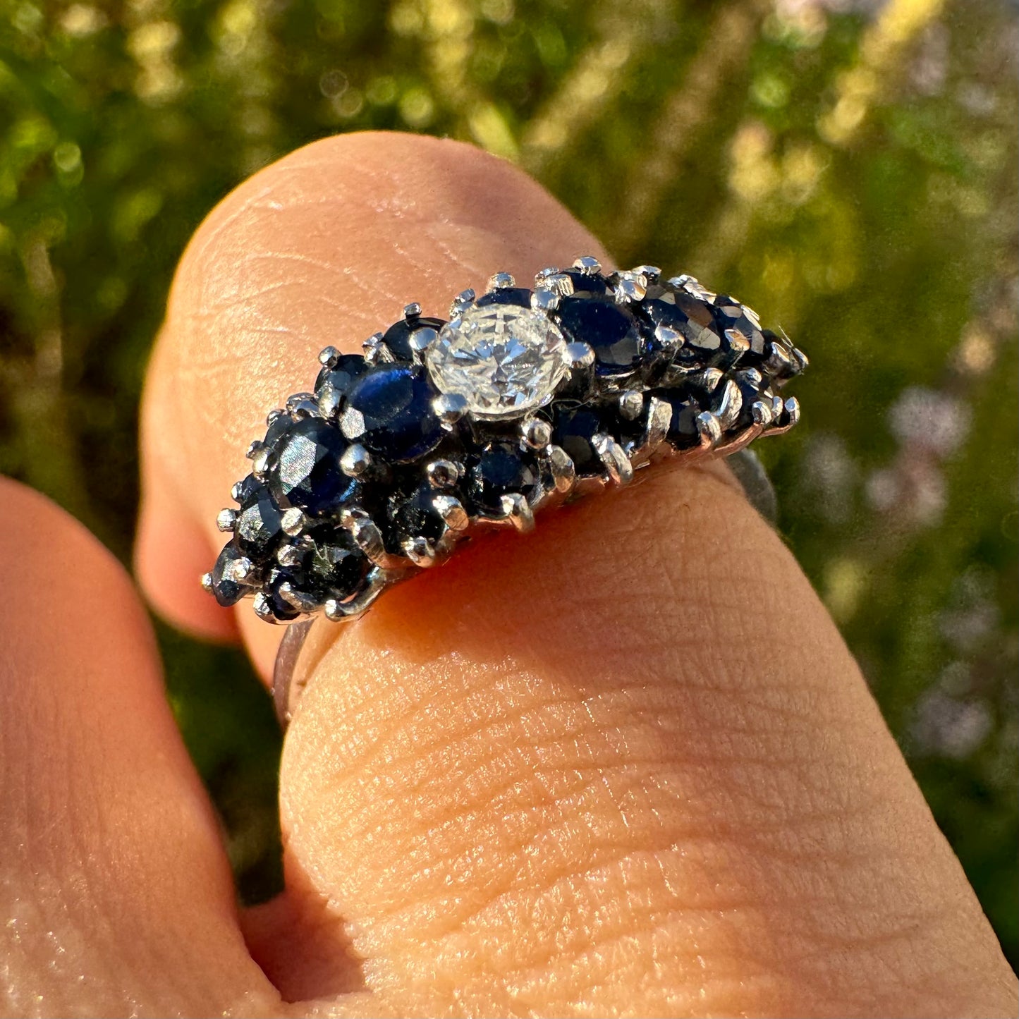 18K gold ring set with a brilliant-cut central Diamond, surrounded by a striking cluster of deep blue Sapphires.