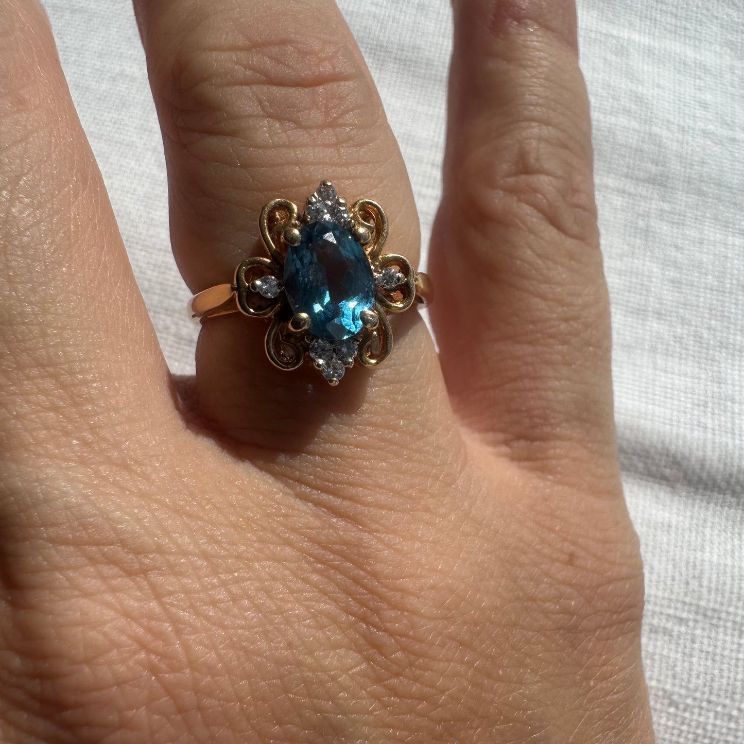 18K gold ring featuring an oval-cut Blue Topaz at the center, accented by sparkling side Diamonds and elegant scroll details.