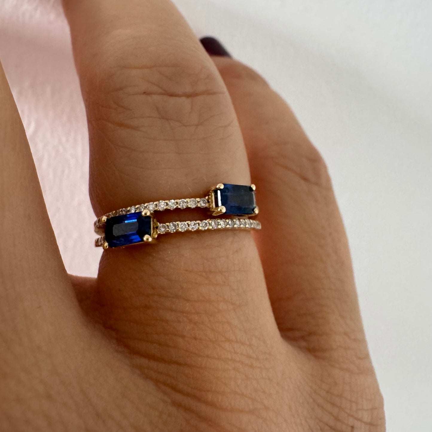 טבעת זהב צהוב 14 קראט בעיצוב פתוח, משובצת שתי אבני ספיר בחיתוך אמרלד ושורות יהלומים עדינים.