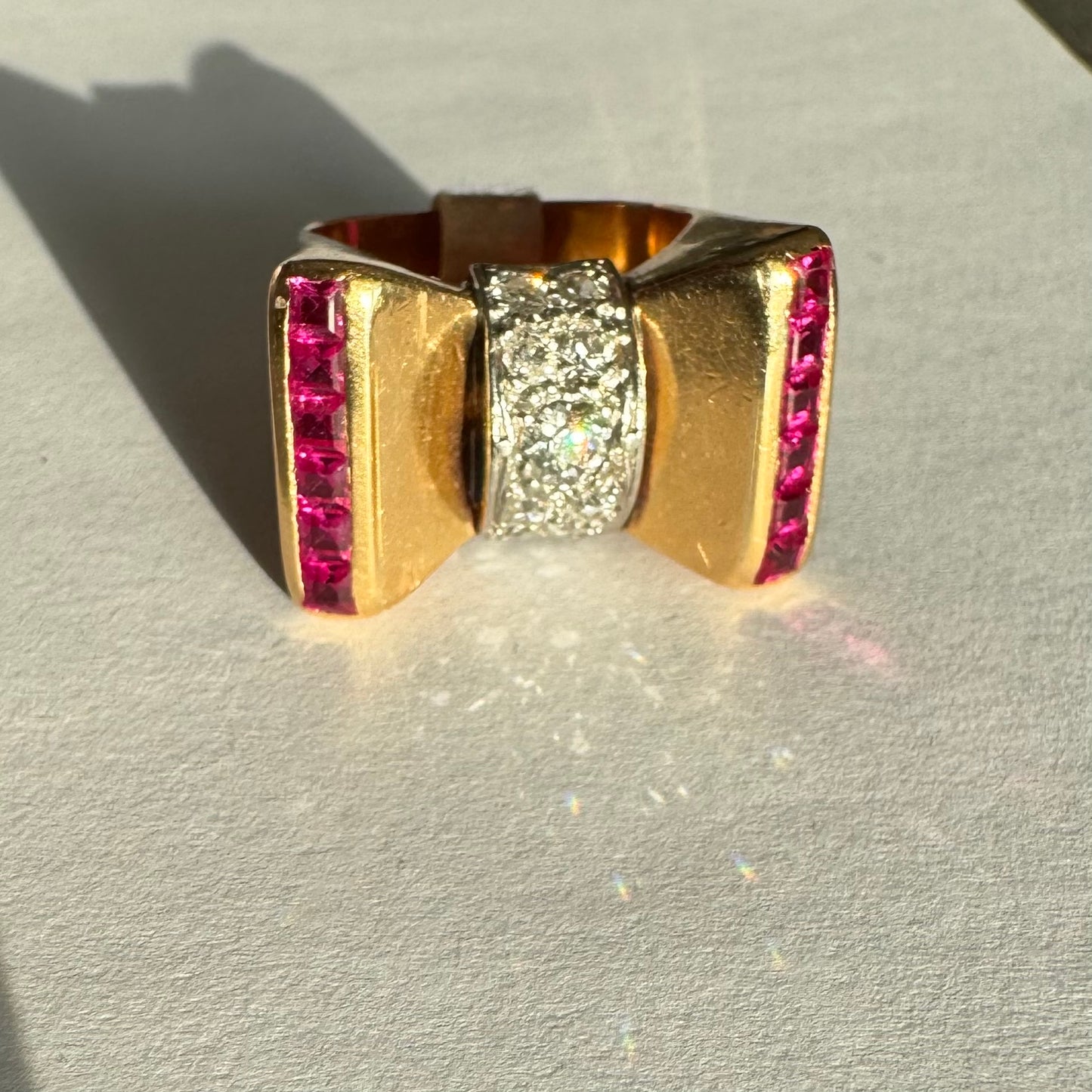 טבעת זהב 18 קראט בצורת פפיון, משובצת יהלומים במרכז ובאבני רובי בחיתוך מרובע בצדדים.