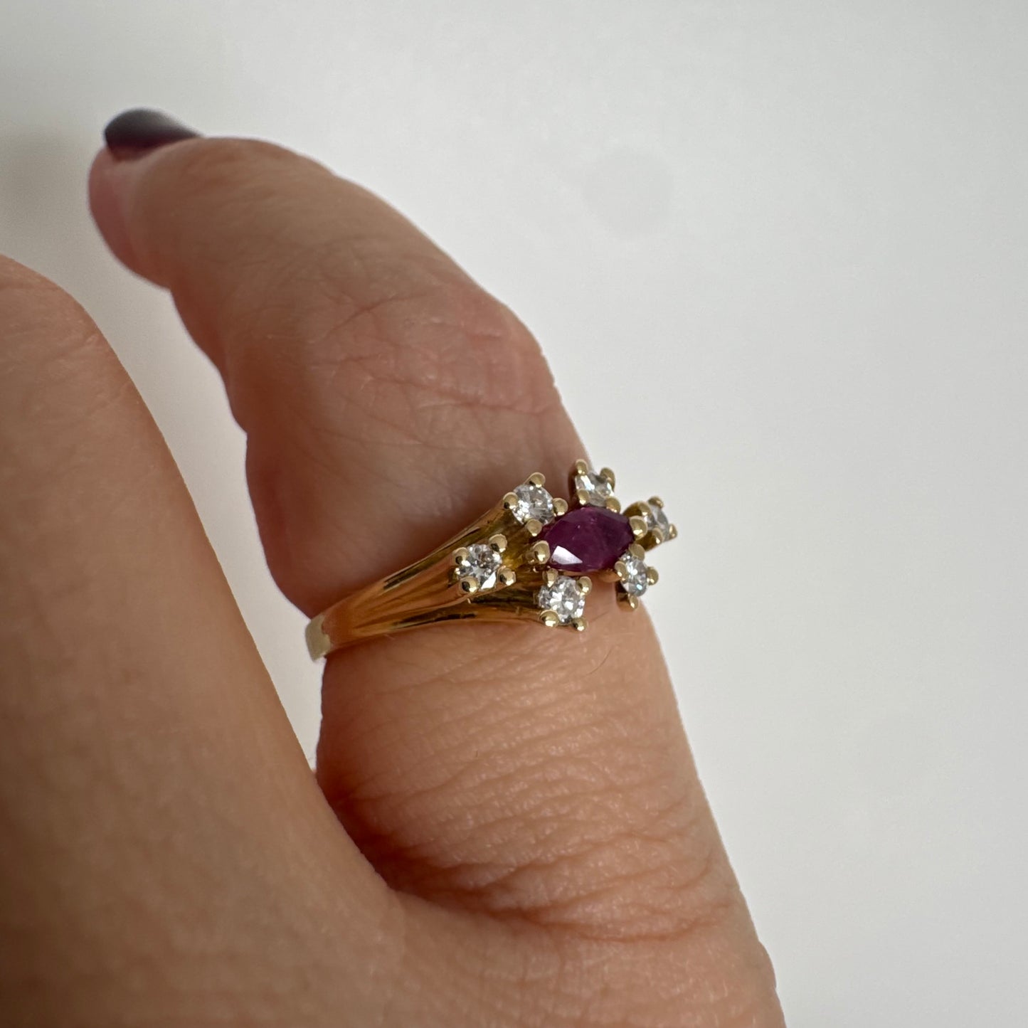 טבעת זהב צהוב 18 קראט משובצת אבן רובי בחיתוך מרקיזה בגוון מוקפת יהלומים בחיתוך עגול משני הצדדים.