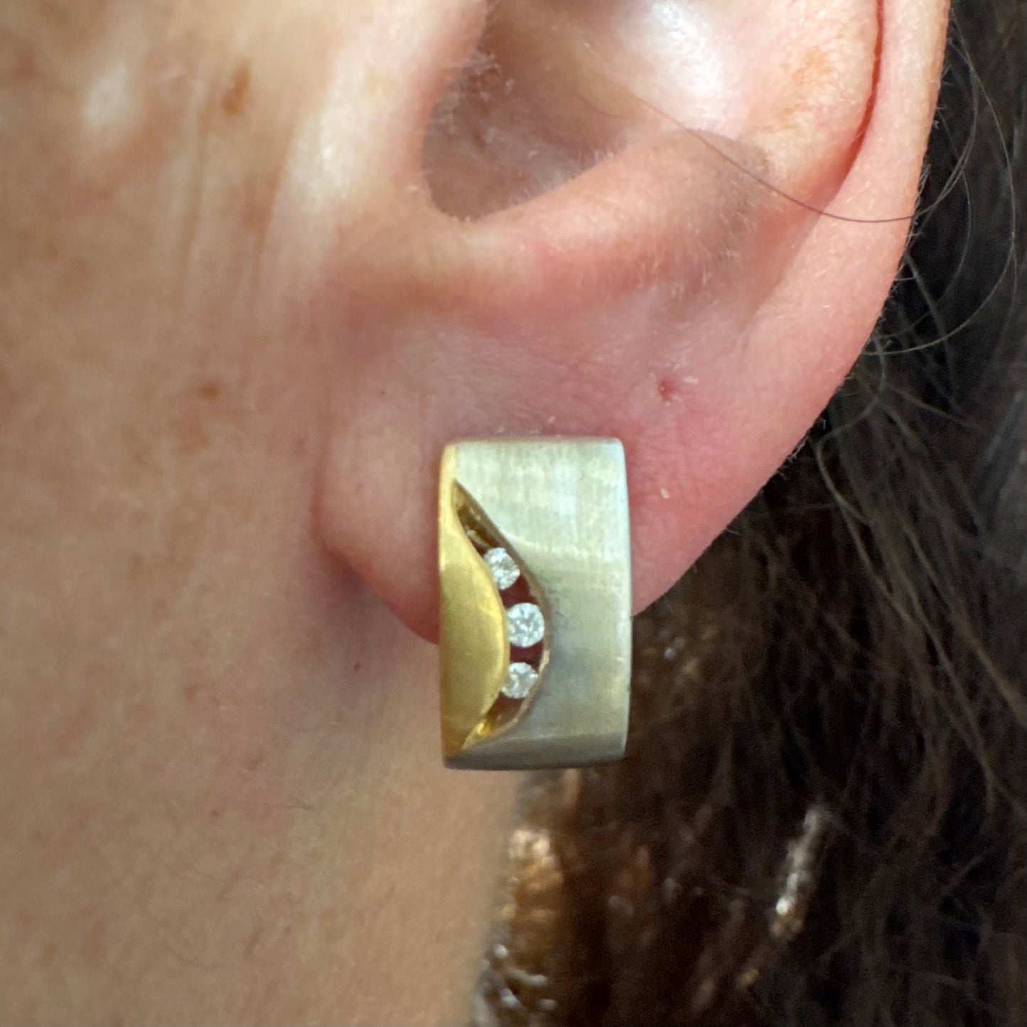 עגילי זהב 18 קראט משובצים יהלומים בעיצוב מודרני ונקי עם שילוב של שני גוונים וגימור מאט יוקרתי.