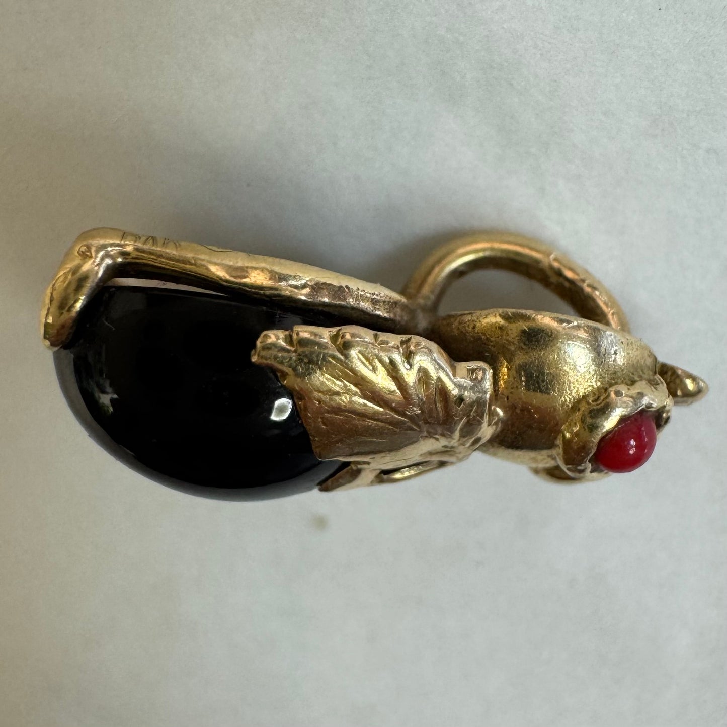 תליון בצורת חיפושית מזהב 14 קראט, עם עיניים אדומות מאבן קורל בחיתוך קבושון וגוף מאבן אוניקס שחורה מבריקה.