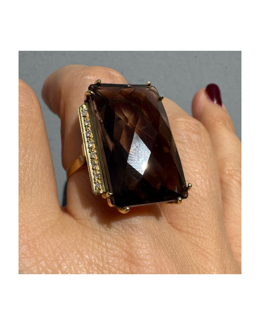 טבעת זהב 18 קראט מרשימה במיוחד בעיצוב סטייטמנט נועז, משובצת אבן סמוקי קוורץ גדולה בחיתוך מלבני עם ליטוש פייסט (faceted) עמוק שמחזיר אור בצורה דרמטית.