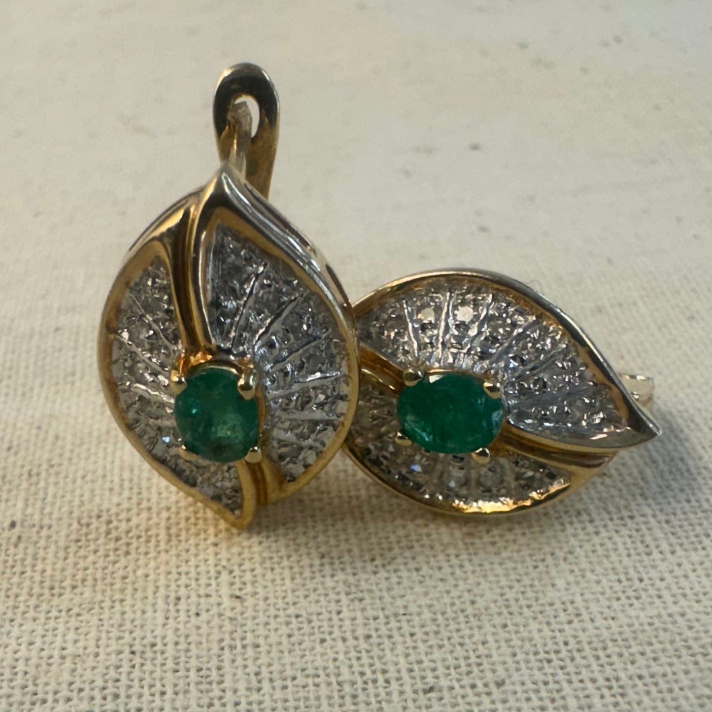 עגילים צמודים לאוזן, זהב צהוב 14 קראט, משובצים אמרלד במרכז, וסביבן פיתוחים משובצים יהלומים, שמעניקים מראה של ניצוץ רך ואלגנטי