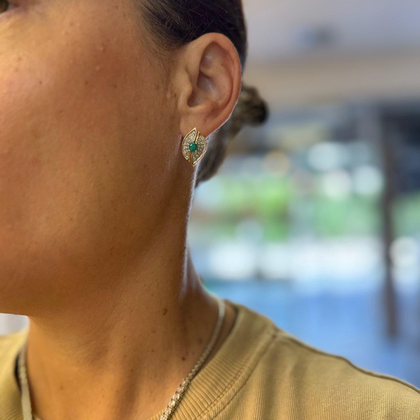 עגילים צמודים לאוזן, זהב צהוב 14 קראט, משובצים אמרלד במרכז, וסביבן פיתוחים משובצים יהלומים, שמעניקים מראה של ניצוץ רך ואלגנטי