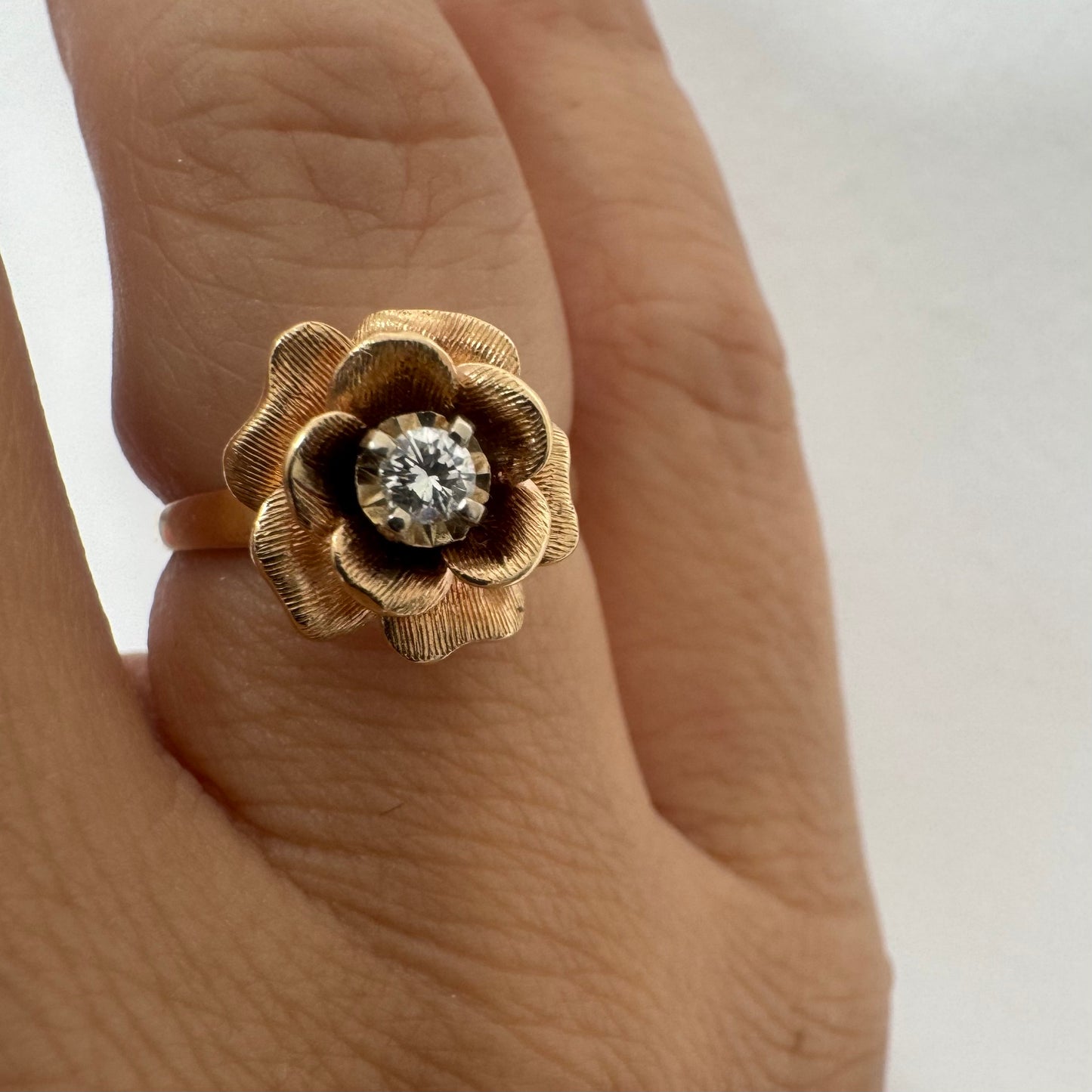 14K Gold floral ring set with delicately textured petals and a sparkling Diamond at the center