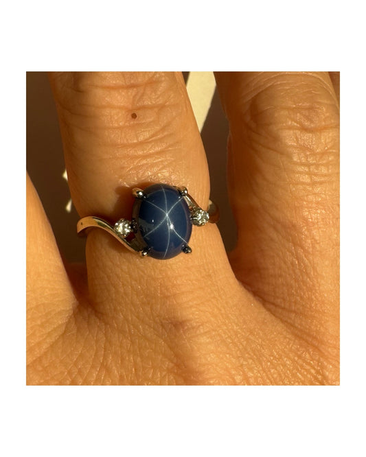 טבעת זהב לבן 14 קראט משובצת אבן ספיר כוכב מרהיבה, המציגה תופעת טבע של שישה קווים זוהרים, ובצידיה שני יהלומים מנצנצים. 