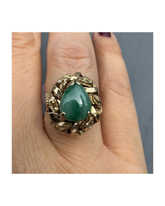 טבעת זהב צהוב 14 קראט משובצת אבן ג׳ייד (ירקן) ירוקה בליטוש קבושון בצורת טיפה (tear drop/pear shape), משובצת בתוך מסגרת זהב עשירה בעיצוב טקסטורות ועלים.